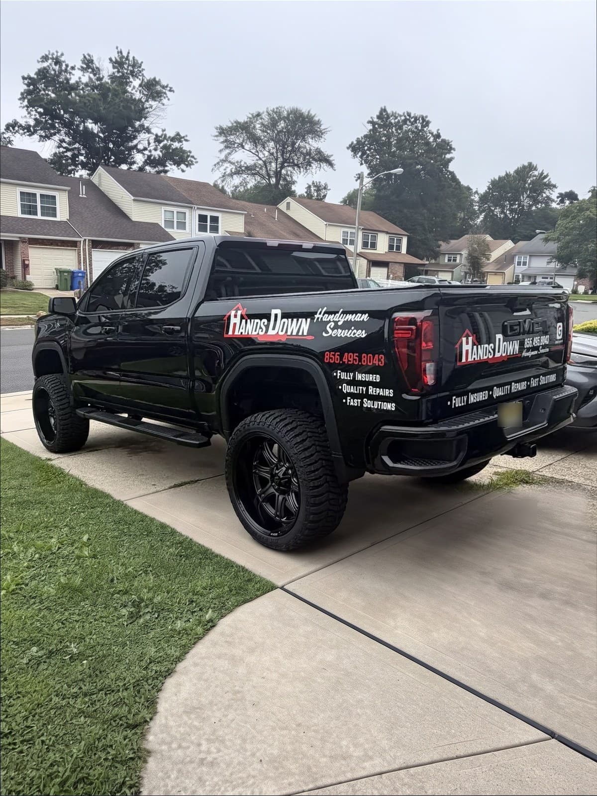 Hands Down Handyman's black GMC pickup parked in a customer's driveway in South Jersey, the logo and (856) 495-8043 lettered on the door