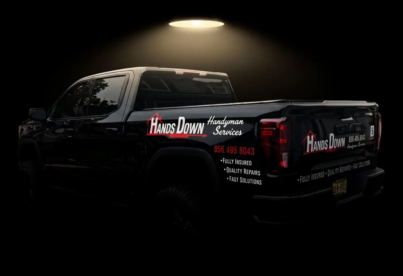 Hands Down Handyman's black GMC pickup under a barn light at night, the logo and (856) 495-8043 lettered on the side